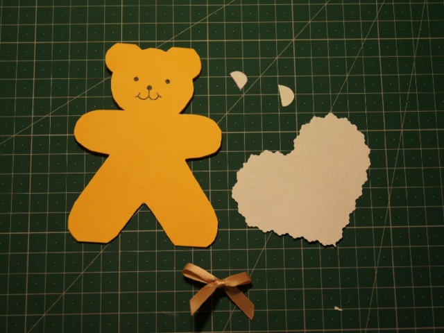 Прорисовываем мордочку медвежонка. Вырезаем из акварельной бумаги по шаблону сердце (фигурными ножницами) и ушки, подготавливаем бантик для украшения.